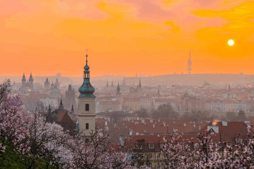 Spring sunrise over Prague with blooming cherry trees, showcasing the cheapest time to visit Europe during shoulder season travel