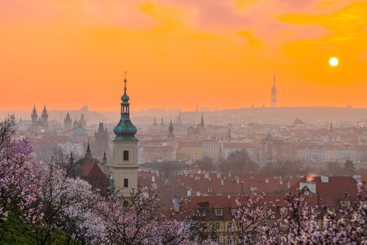 Spring sunrise over Prague with blooming cherry trees, showcasing the cheapest time to visit Europe during shoulder season travel