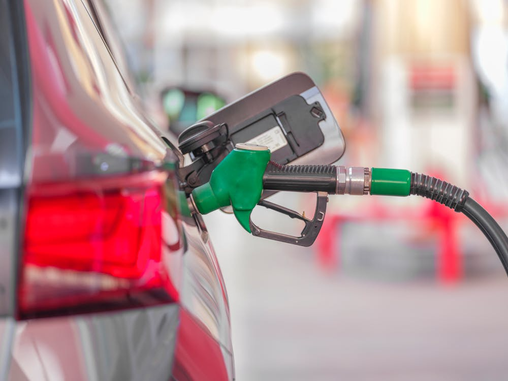 Close-up of a car being refueled at a gas station with a green nozzle